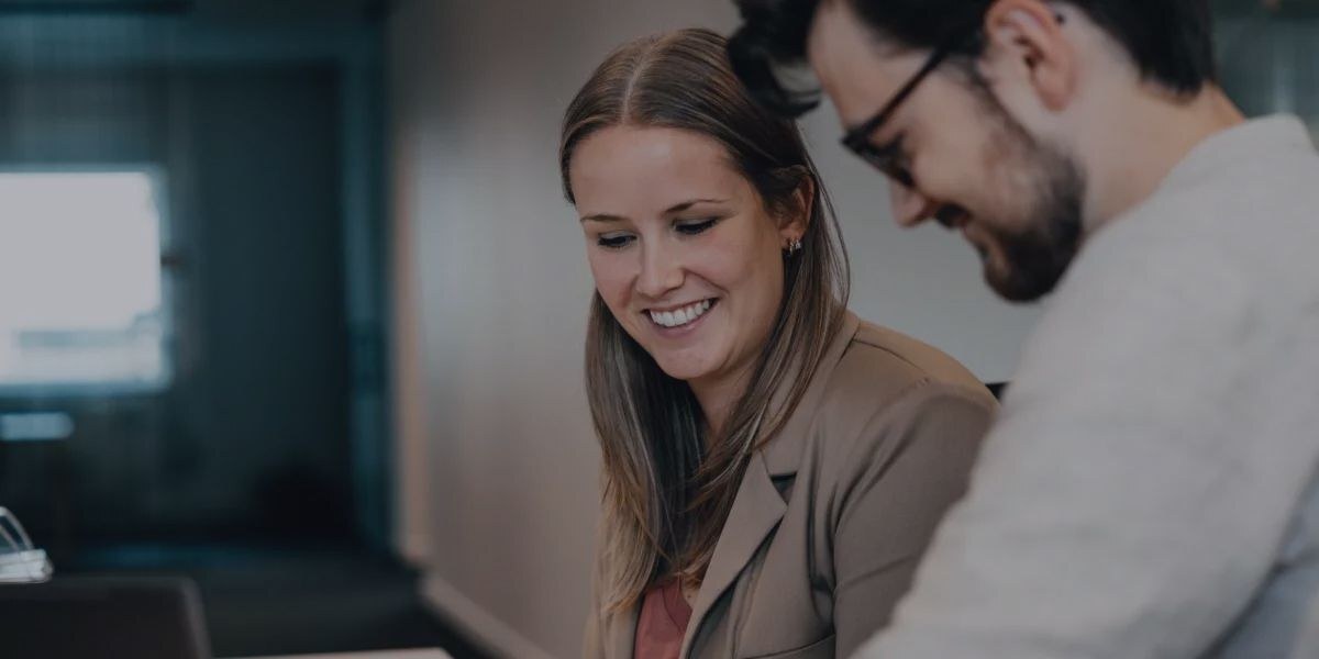 Twee collega's kijken lachend samen naar een scherm